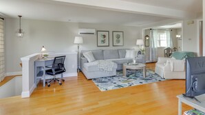 A spacious living room with a grey sofa, a white armchair, a coffee table, and a TV on a stand. There is a desk with a chair and a lamp, and a patterned rug on the floor. - Walk to Beaches: Sunny East Haven Home w/ Grill (East Haven)