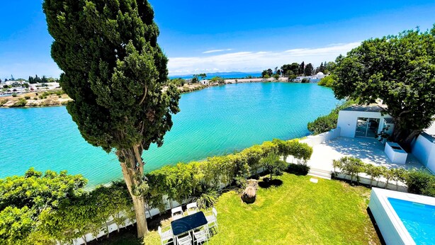 A poolside area with a table and chairs, a small building, and a view of a large body of water. - Villa Punique Villa Exceptionnelle Avec vue mer (Carthage)
