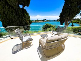 Varanda com mobiliário de vime com vista para um mar azul límpido e vegetação exuberante.