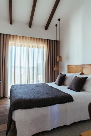 A bedroom with a large bed, wooden beams on the ceiling, and a view through sheer curtains. - Two Bedroom Apartment (Zambujeira do Mar)