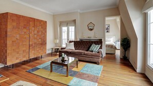 Ein Wohnzimmer mit einem braunen Sofa, einem Holzschrank, einem Couchtisch und einem farbenfrohen Teppich.