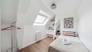 Un dormitorio moderno con tragaluz, una cama con una toalla enrollada, una percha para ropa y un radiador blanco.