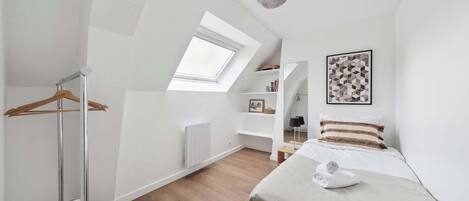 A modern bedroom with a skylight, a bed with a rolled towel, a hanging clothes rack, and a white radiator.