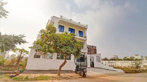 A modern two-story building with a white facade, a tree in the foreground, and a parked motorcycle. - Hotel Olive Tree (Agra)