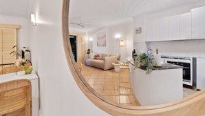 A modern kitchen with white cabinets, a dining area with wicker chairs, and a living room with a beige sofa. - Cozy Waterfront - Free Parking Pool (Cairns North)