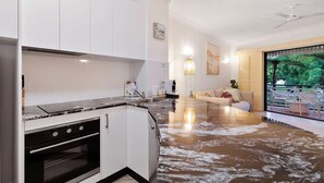 A modern kitchen with white cabinetry, a black stove, and a large island with a marble countertop. - Cozy Waterfront - Free Parking Pool (Cairns North)