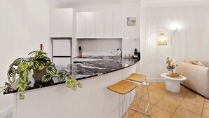 A modern kitchen with white cabinets, a black marble countertop, and a small island with stools. - Cozy Waterfront - Free Parking Pool (Cairns North)