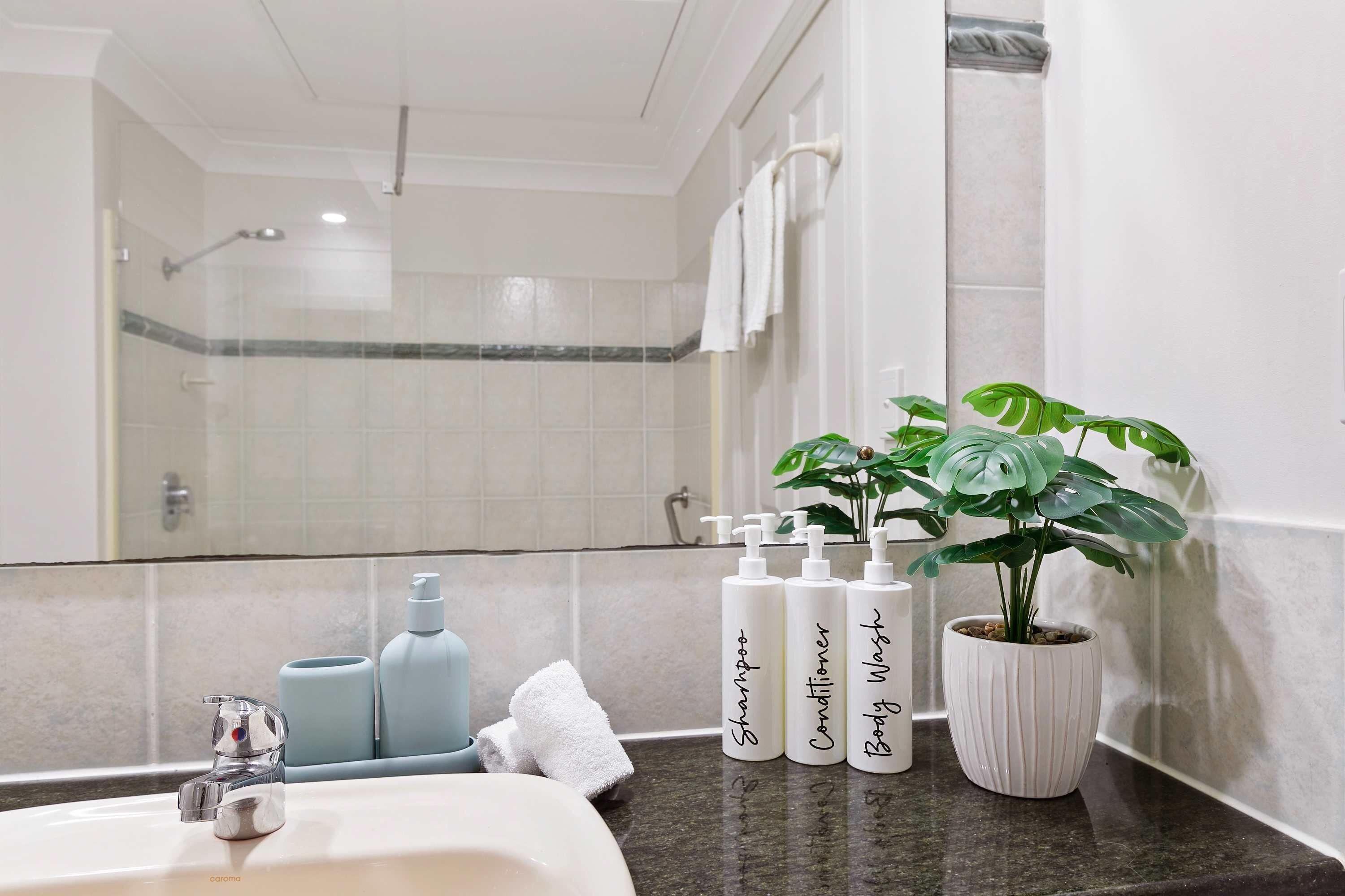 A bathroom with a sink, mirror, and toiletries including shampoo, conditioner, and body wash.
