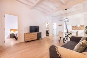 Een moderne woonkamer met een houten vloer, een televisie op een houten kast, een bank en een eethoek met een tafel en stoelen.