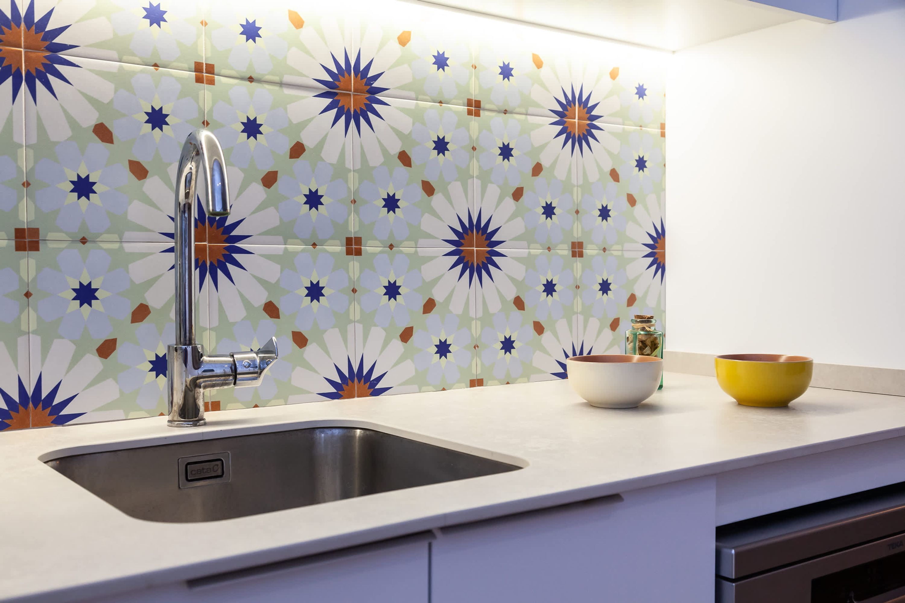 A kitchen with a modern sink, white cabinets, and a decorative backsplash.