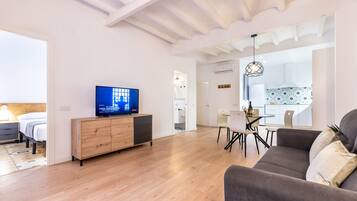 Una sala moderna con un mueble de madera, un televisor de pantalla plana, un sofá gris y un comedor con mesa y sillas.