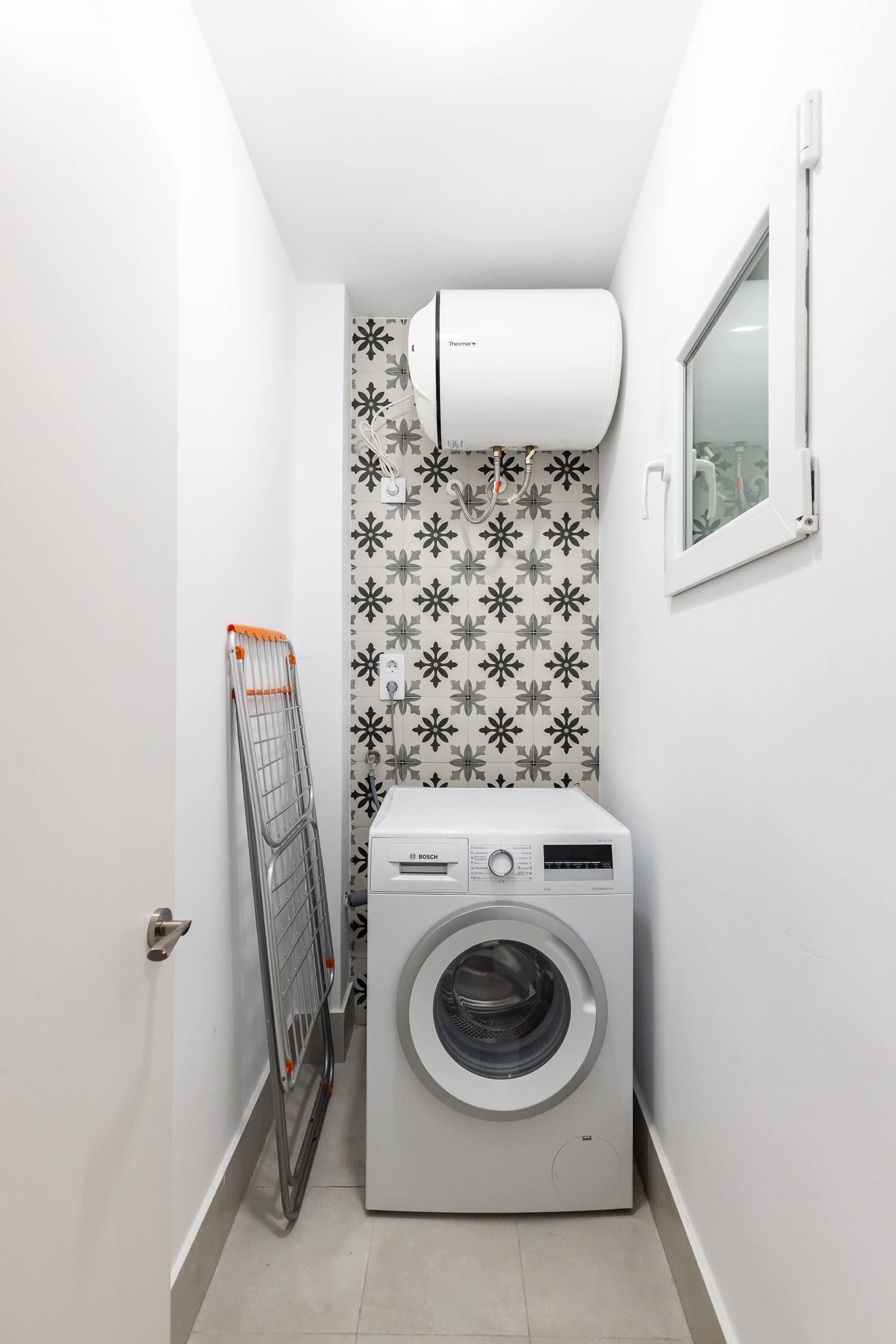 Un lavadero pequeño con una lavadora Bosch, un tendedero y un aire acondicionado de pared.