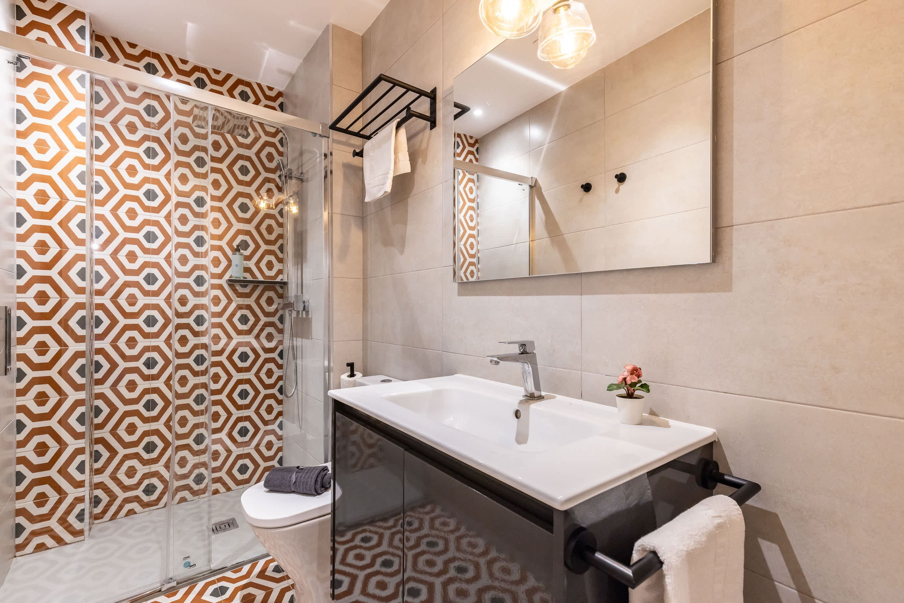 Un baño moderno con cabina de ducha de vidrio, un lavabo blanco y un espejo grande.