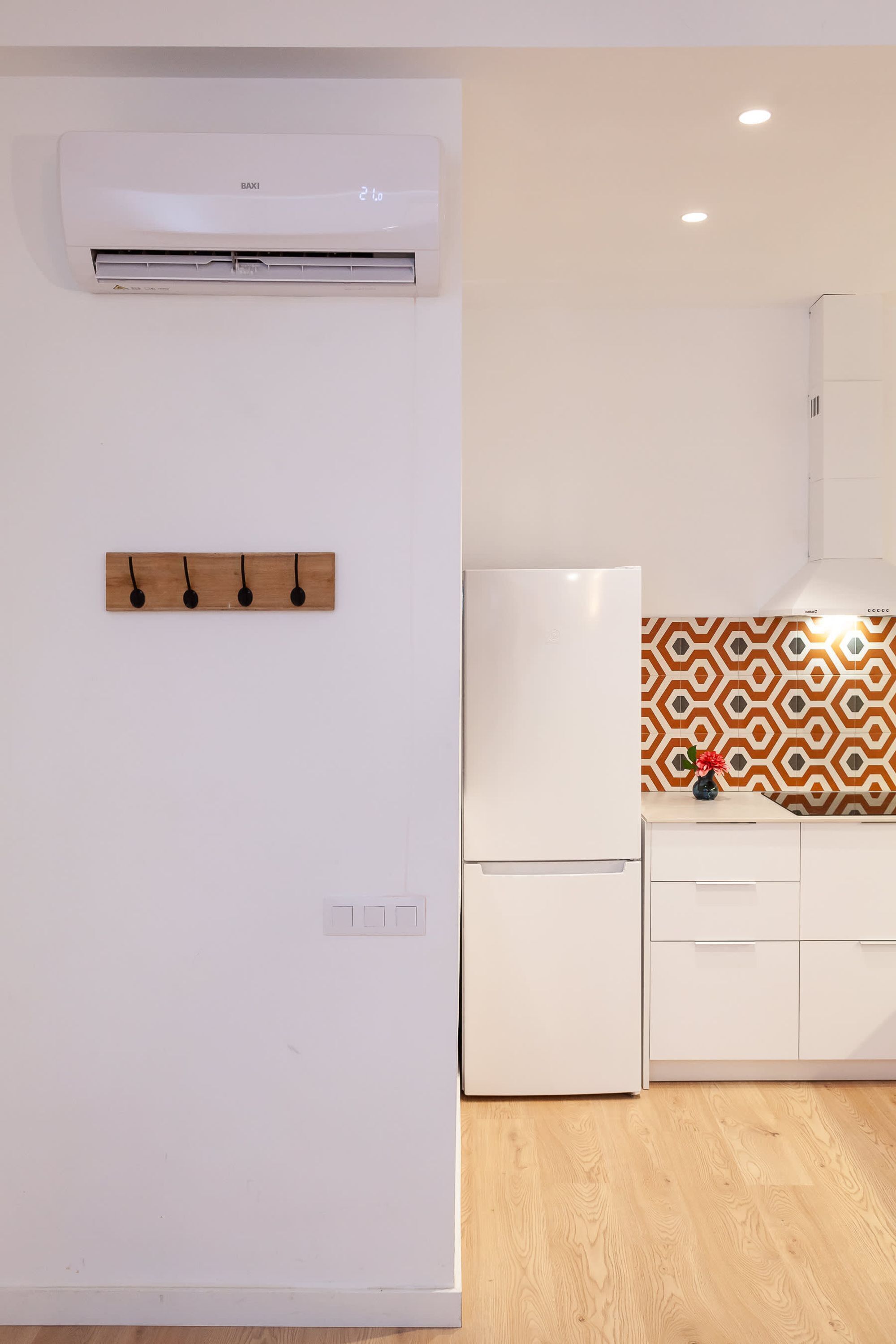 Cocina con refrigerador blanco, aire acondicionado de pared y panel de madera con tres ganchos.