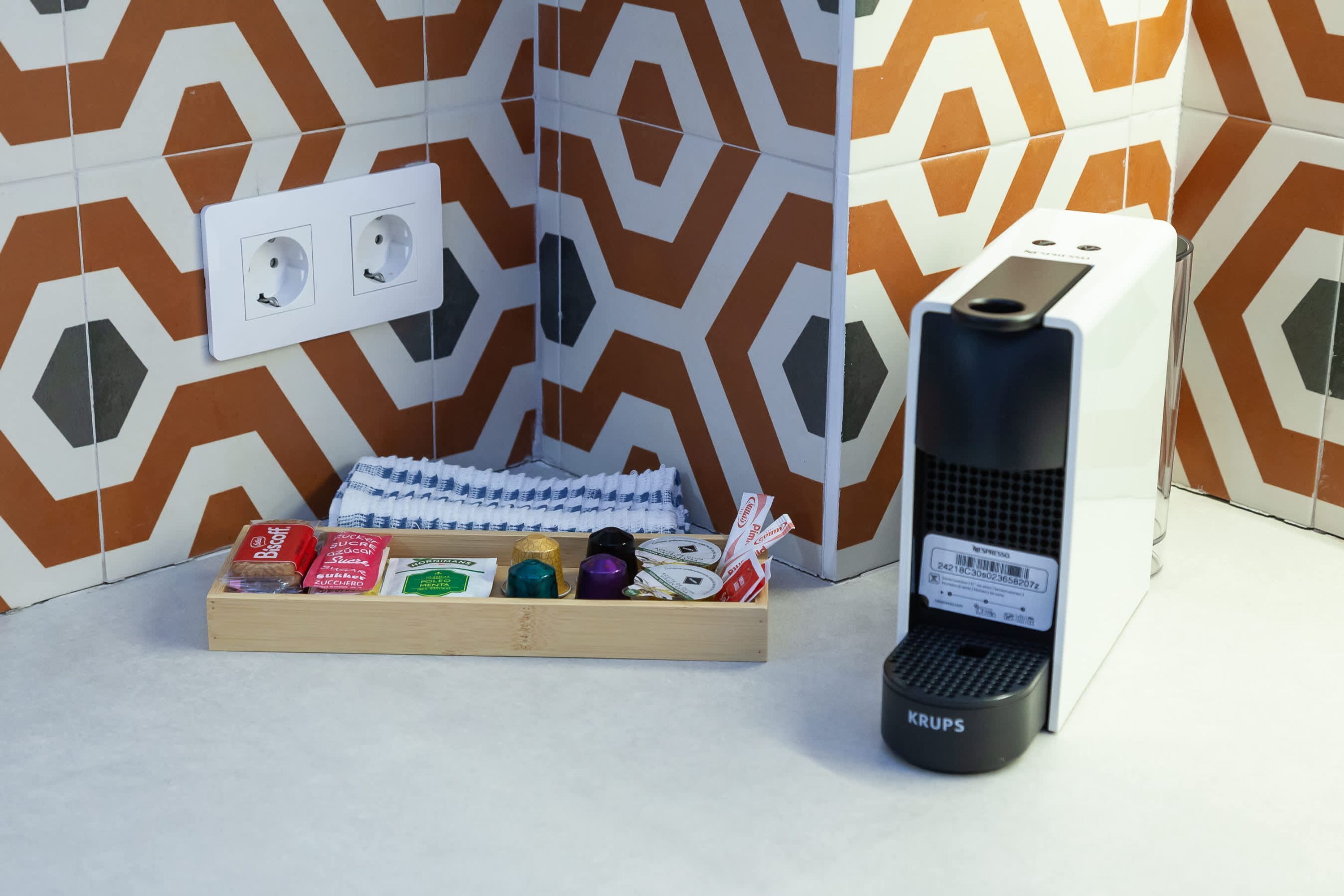 A bathroom with a geometric patterned tile wall, a wooden tray with toiletries, and a black Krups electric toothbrush.