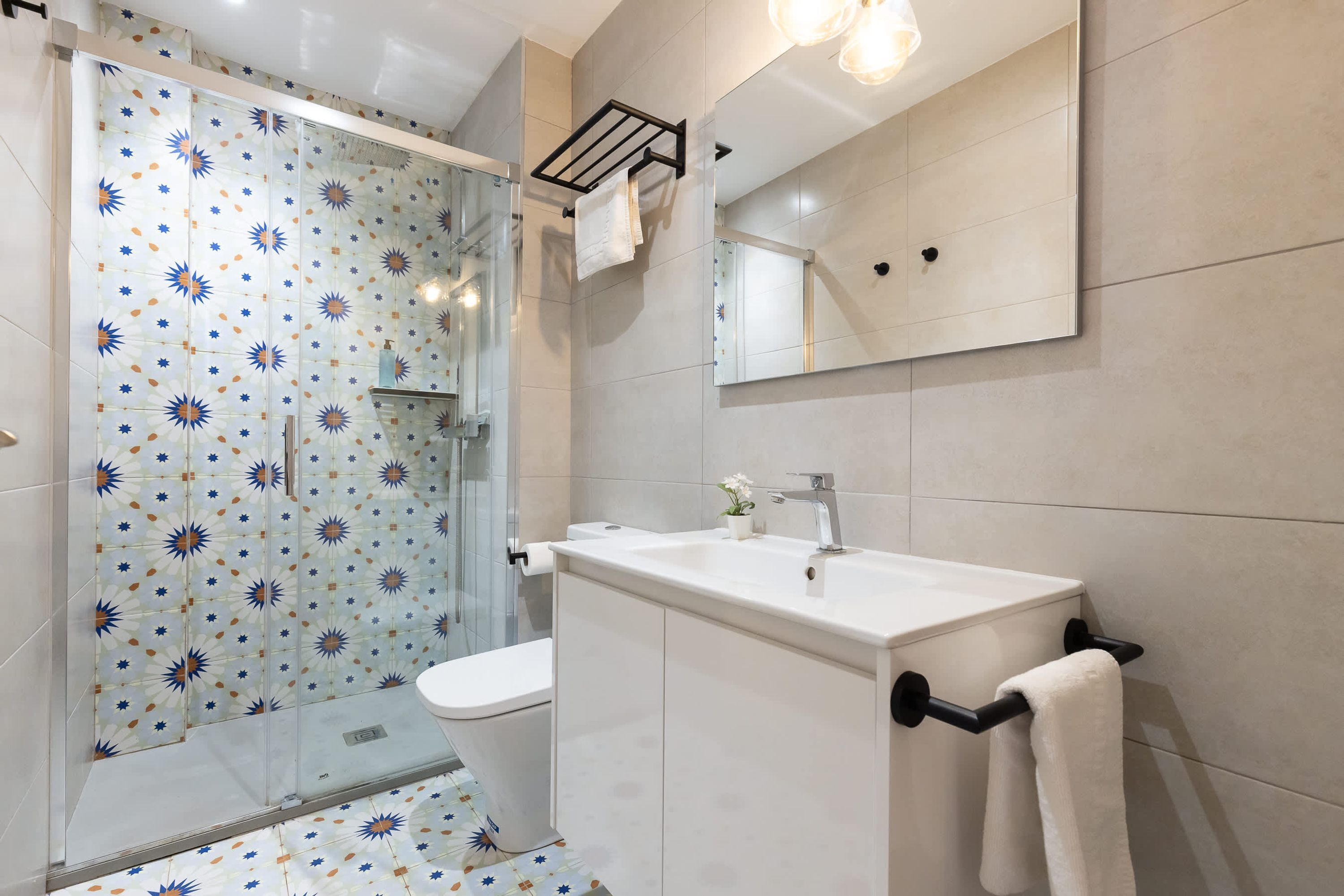Un baño moderno con cabina de ducha de vidrio, inodoro blanco y lavamanos con toallero.