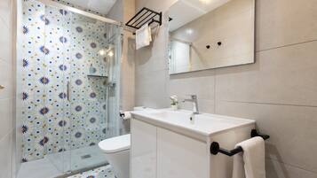 Un baño moderno con cabina de ducha de vidrio, inodoro blanco y lavamanos con toallero.