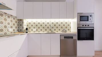 Una cocina moderna con armarios blancos, lavavajillas de acero inoxidable y horno empotrado.