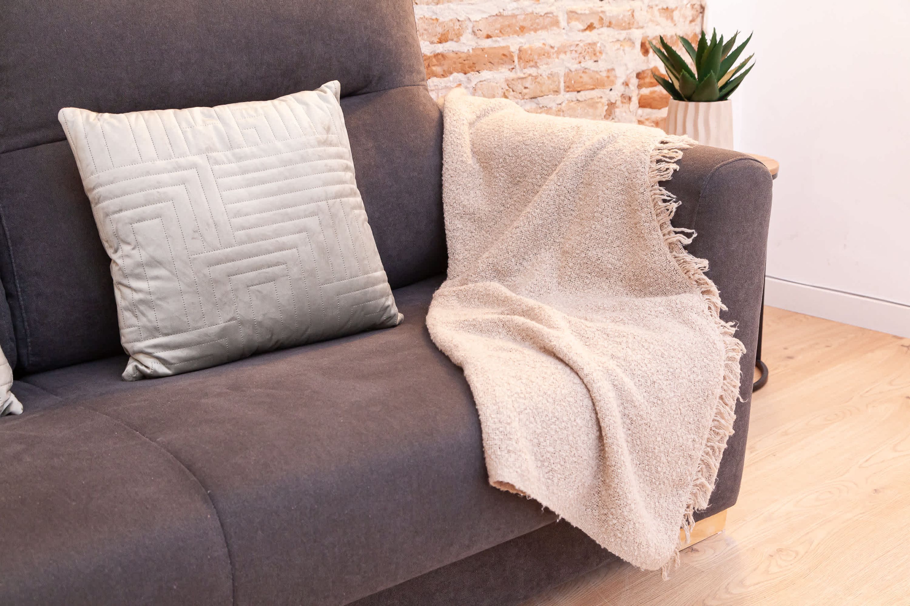 Un sofá gris con una manta color beige y una almohada acolchada blanca.