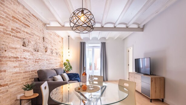 A modern living room with a glass dining table, a sofa, a TV, and a brick wall. - Unik Vacation Cavallers (Tarragona)