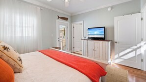 A bedroom with a bed, a television on a cabinet, a ceiling fan, and a view of the outside.