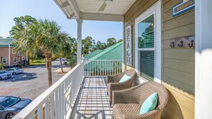 A covered porch with wicker chairs and a ceiling fan, overlooking a street with parked cars and palm trees.