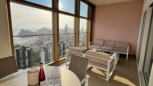 Ein modernes Wohnzimmer mit großem Fenster, einem Esstisch mit Flasche und Gläsern sowie einer Sofagarnitur.