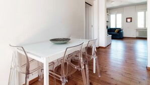 Un moderno comedor con una mesa blanca y sillas transparentes, un bol en la mesa y un sofá azul al fondo.