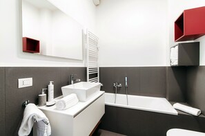 Ein modernes Badezimmer mit einem weißen Waschtisch, einem großen Spiegel, einer Badewanne und einem roten Regal.