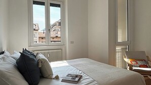 Un dormitorio con cama, almohadas, una silla, una ventana y un radiador.