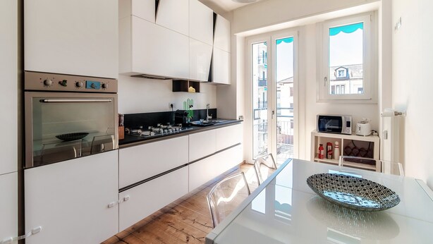 Una cocina moderna con armarios blancos, un horno de acero inoxidable y una mesa de comedor de vidrio.