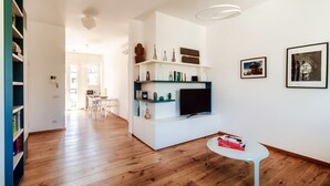 Un salón moderno con suelo de madera, paredes blancas, un televisor de pantalla plana y una mesa de centro blanca.