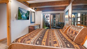 Un dormitorio con una cama grande, techo de madera, un cuadro de un paisaje, una silla y vistas al exterior.