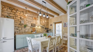 Eine rustikale Küche mit Steinwand, Holzbalken und einer Essecke mit weißem Tisch und Stühlen.