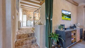 A staircase leading to a kitchen area with stone flooring, a wooden ceiling, and a green curtain.
