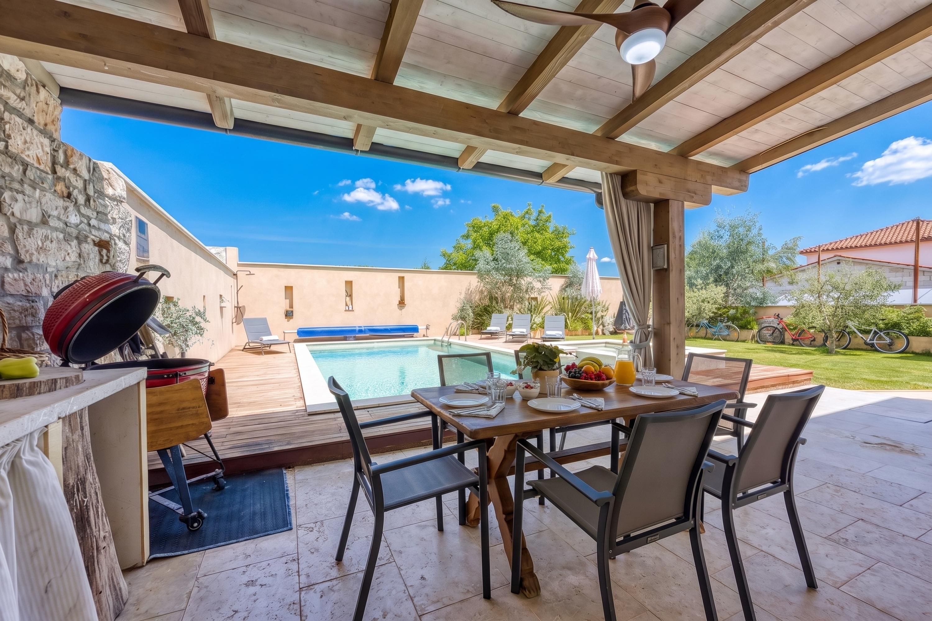 An outdoor patio with a pool, dining table, chairs, and a barbecue grill.