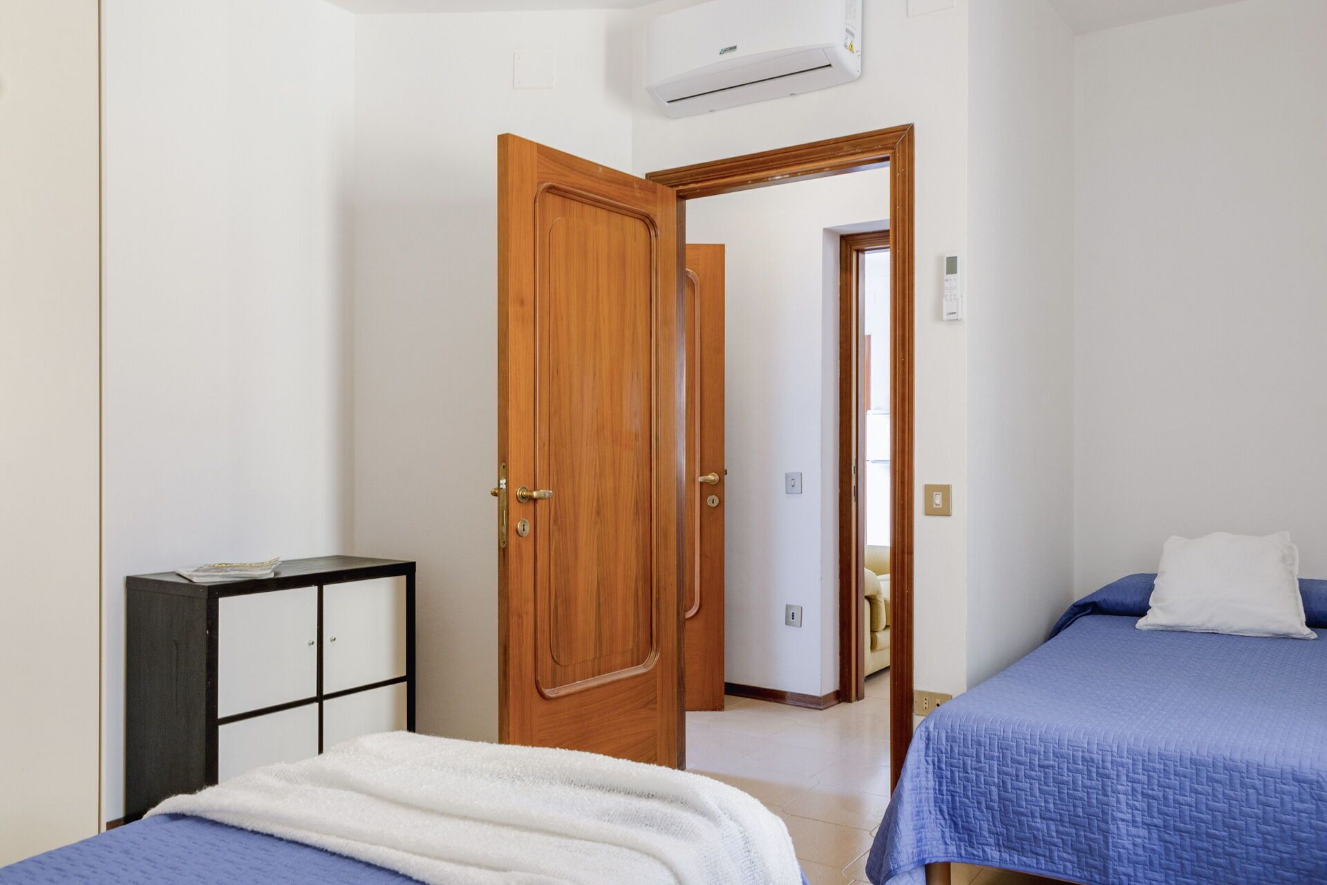 A bedroom with two beds, a wardrobe, and a small table.