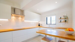 A modern kitchen with white cabinets, wooden countertops, and a built-in oven. There is a window providing natural light and a bowl of fruit on the counter. - 91A Casa Mel: Stylish 3-Bed Townhouse with Pool (Carvoeiro)