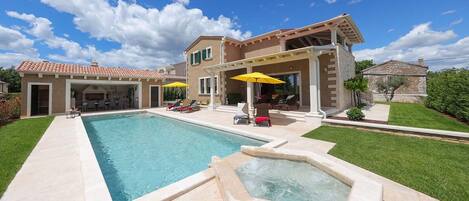 Una piscina amplia con jacuzzi, mobiliario exterior y un patio cubierto.