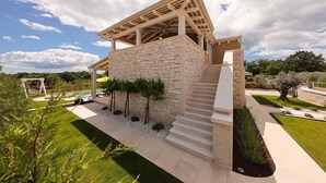 Ein modernes Haus mit Natursteinfassade, einer Holzpergola und einem gepflegten Rasen.