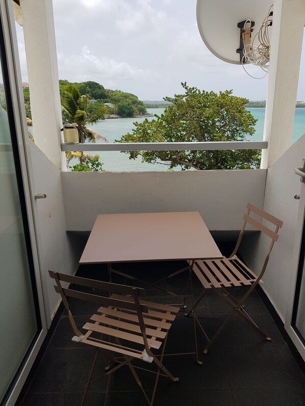 A balcony with a table and two chairs, overlooking a body of water and greenery.