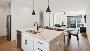 Une cuisine moderne dotée d’un plan de travail en granit, d’appareils électroménagers en acier inoxydable et de luminaires suspendus.