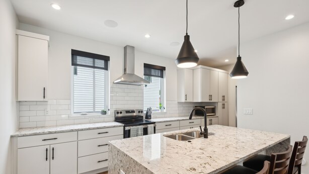 Une cuisine moderne avec des armoires blanches, un îlot en granit et des luminaires suspendus.