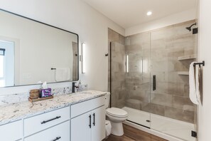Un bagno moderno con un piano d'appoggio in marmo, un water, una cabina doccia in vetro e uno specchio grande.