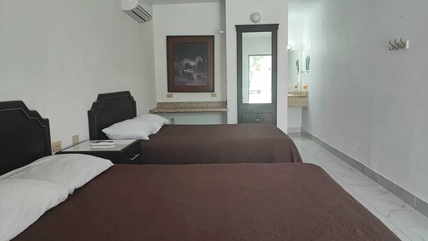 A hotel room with two beds, a framed picture on the wall, a mirror, and a bathroom visible through an open door. - Hotel Estrella Matamoros (Matamoros)