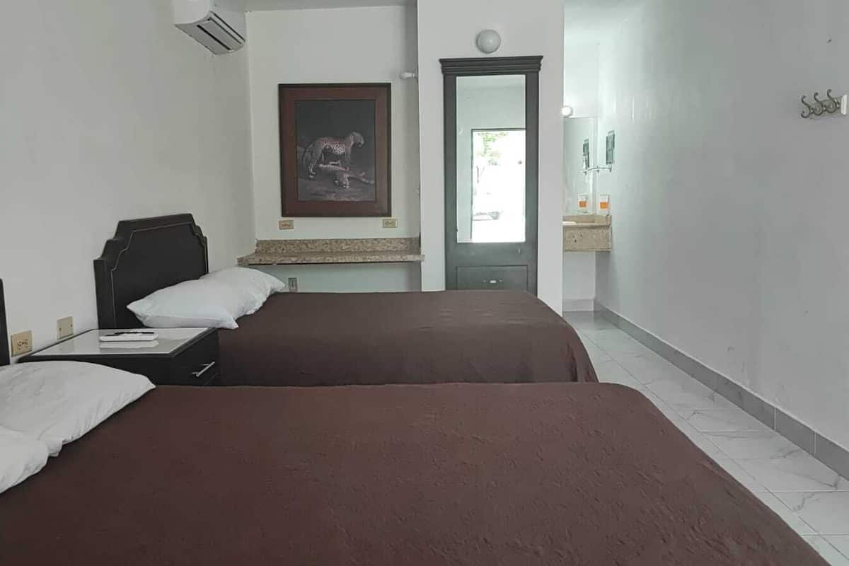 A hotel room with two beds, a framed picture on the wall, a mirror, and a bathroom visible through an open door.