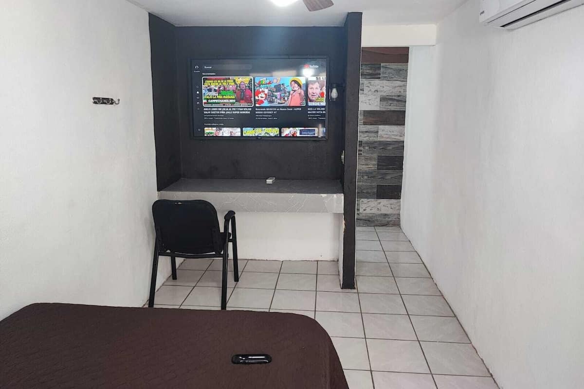 A room with a bed, a TV mounted on the wall, a ceiling fan, and an air conditioning unit.