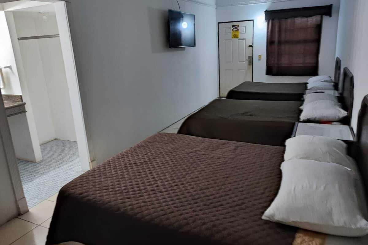 A hotel room with two single beds, a television mounted on the wall, and a door with a sign.