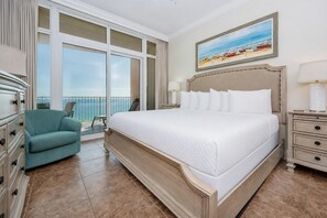 A hotel room with a large bed, a chair, a nightstand, and a painting of a beach scene. - Phoenix Gulf Shores 803 3 Bedroom Condo by RedAwning (Gulf Shores)