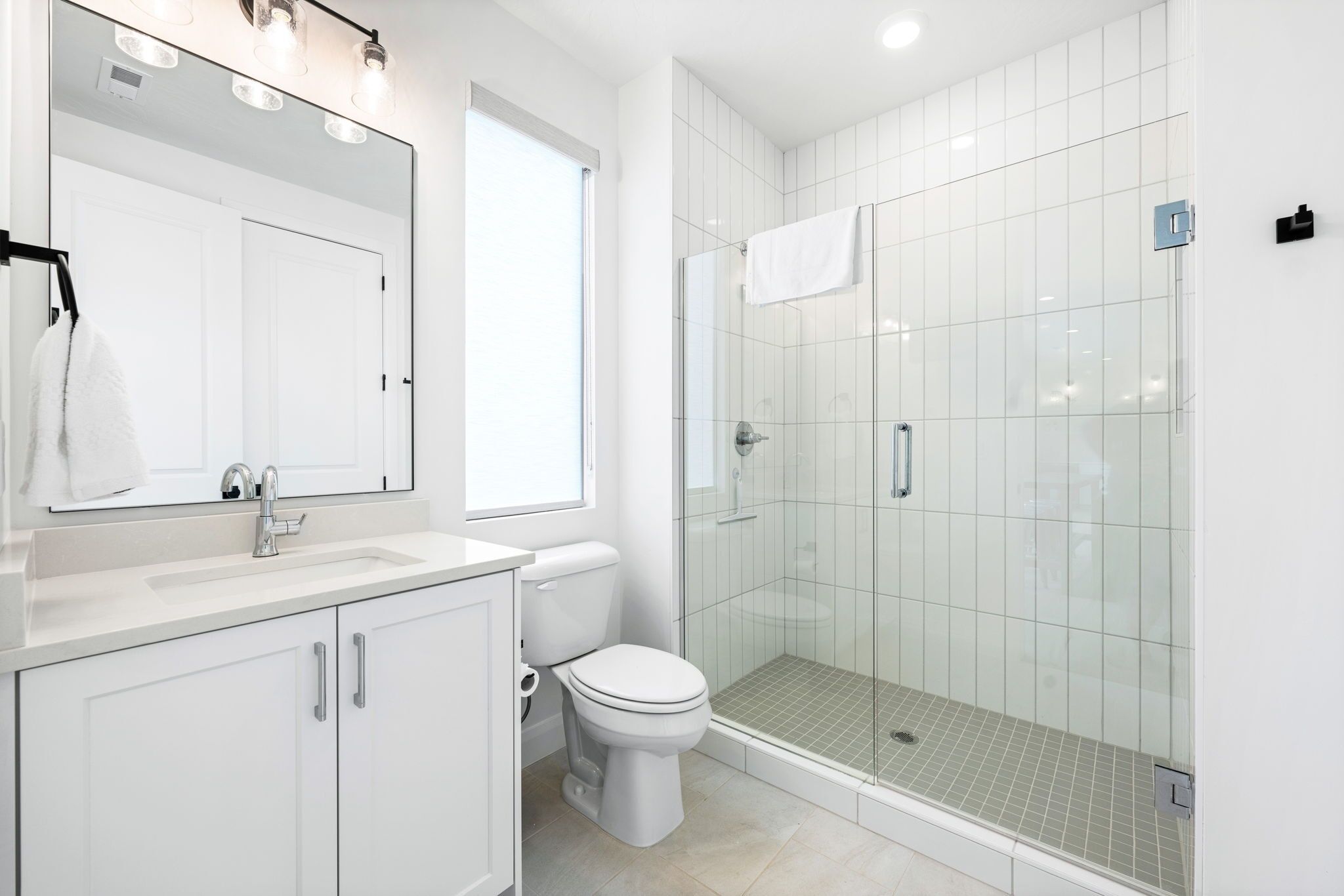 Une salle de bain moderne avec un lavabo blanc, un miroir, des toilettes et une douche à parois de verre.